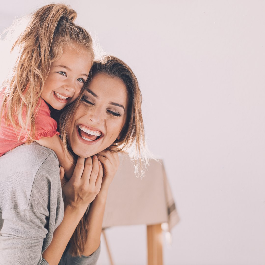 A mom laughing with her daughter on her back
